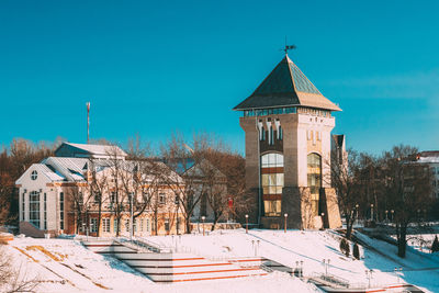 Building by snow covered trees against blue sky