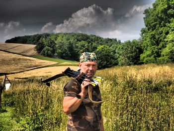 Portrait of archer standing on grassy field against trees