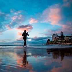 Low angle view of silhouette person walking at beach against cloudy sky at dawn