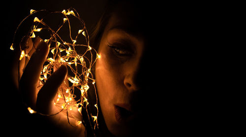 Close-up of woman holding christmas lights against black background