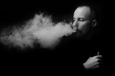 Man smoking electronic cigarette against black background