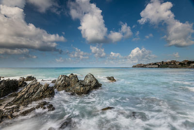 Rock formations by sea against cloudy sky