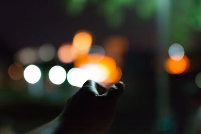 Cropped image of hand reaching towards illuminated lights at night