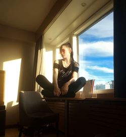 Young woman looking through window at home