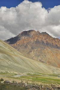 View of a beautiful rocky mountain with clouds in sky and flowing a river