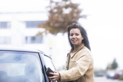 Portrait of smiling woman standing by car in city