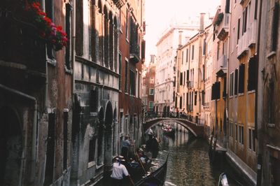 People sitting in gondola at canal amidst buildings in city