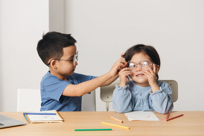 Boy helping sister to wear eyeglasses at home