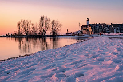 Snow covered buildings and trees against sky during sunset