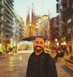 Portrait of smiling man standing against sagrada familia in illuminated city