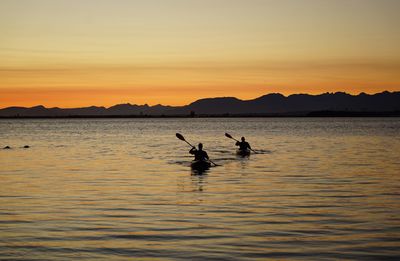 Silhouette people on sea against sky during sunset