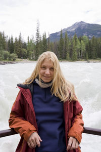 Portrait of young woman standing at observation point against river