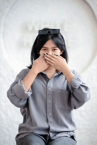 Young woman using mobile phone while standing against wall