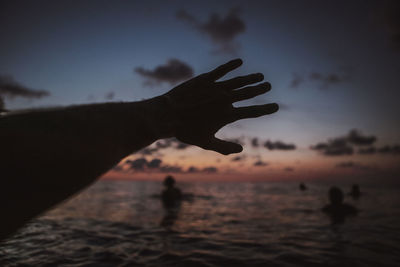 Silhouette hand against sea during sunset