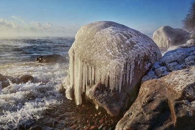 Close-up of frozen sea by rocks against sky during winter