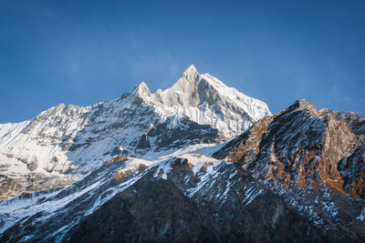 Low angle view of snowcapped mountains against clear blue sky