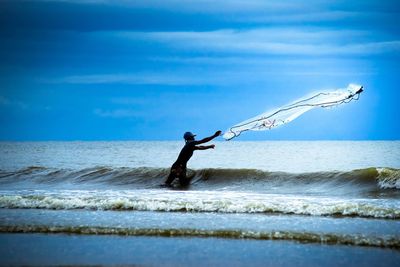 Man reaching fishing net in sea against sky