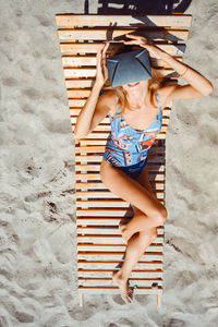 Young woman using virtual reality simulator while sitting on lounge chair at beach