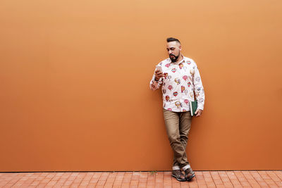 Bearded man leaning on wall while using smartphone by office building