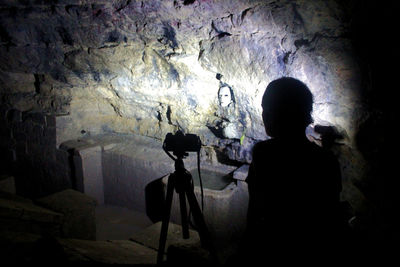 Rear view of silhouette man photographing in cave