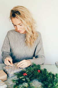 Young blonde woman wraps a christmas present.  christmas wreath made of fir branches.