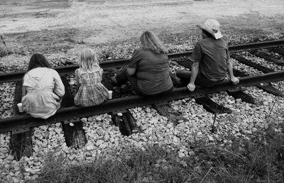 Rear view of people sitting on railroad tracks