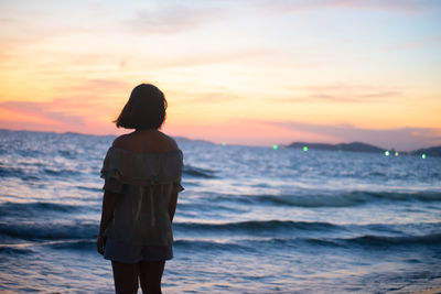 Rear view of woman standing on beach during sunset