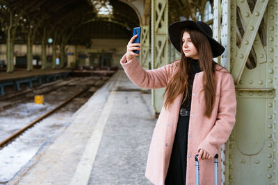 Happy young woman on platform of railway station in pink coat and black hat