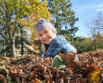 Portrait of girl on leaves against trees and sky