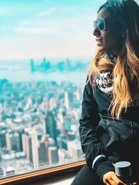 Woman looking through window against cityscape