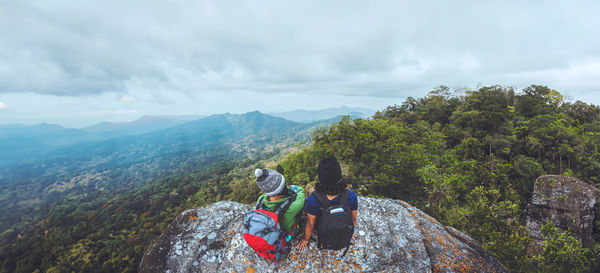 Rear view of man sitting on mountain against sky