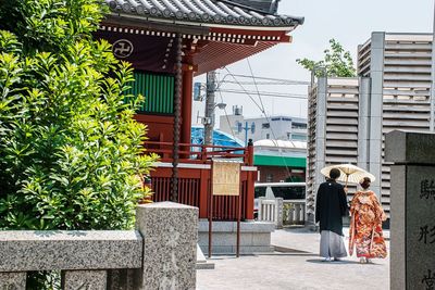 Rear view of man and woman walking with umbrella by building