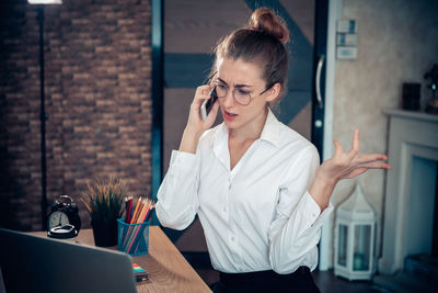 Young woman using mobile phone while sitting on table