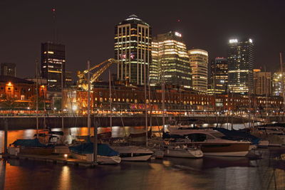 Boats moored in harbor against illuminated buildings in city at night