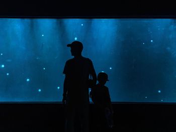 Rear view of silhouette man looking at aquarium