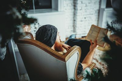 High angle view of man reading book while sitting on arm chair