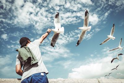 Low angle view of man feeding seagull flying in sky