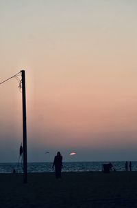 Rear view of silhouette people on beach against sky during sunset
