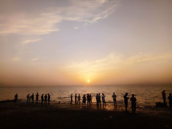 Silhouette people standing at beach during sunset