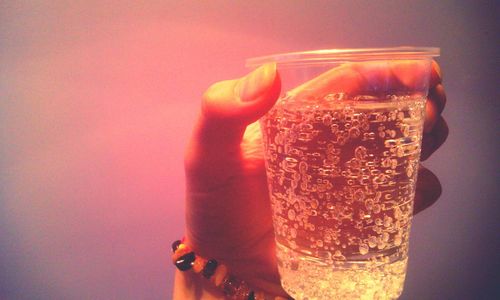 Close-up of hand holding drink against gray background