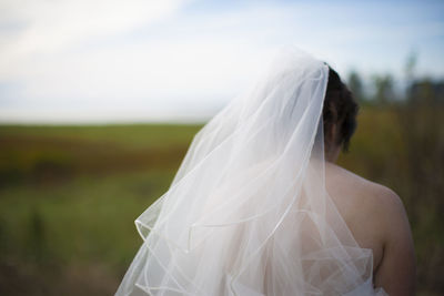 Rear view of bride standing on field against sky