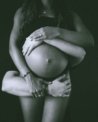 Rear view of shirtless young woman standing against black background