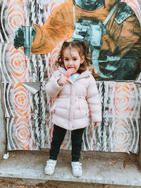 Full length portrait of cute girl standing against graffiti