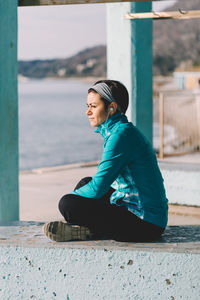 Side view of young woman sitting on retaining wall