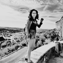 Full length portrait of young woman standing against sky