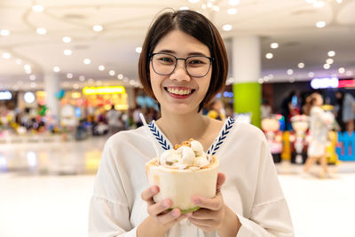 Portrait of smiling woman holding ice cream at shopping mall