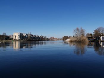 Buildings by lake against clear blue sky