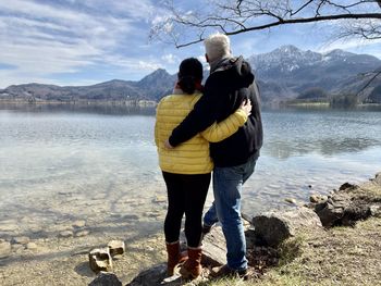 Rear view of couple standing at lakeshore against sky