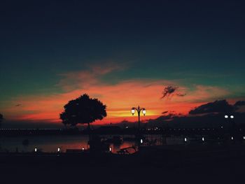 Silhouette trees by sea against sky during sunset