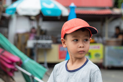 Cute boy wearing cap looking away while standing on road